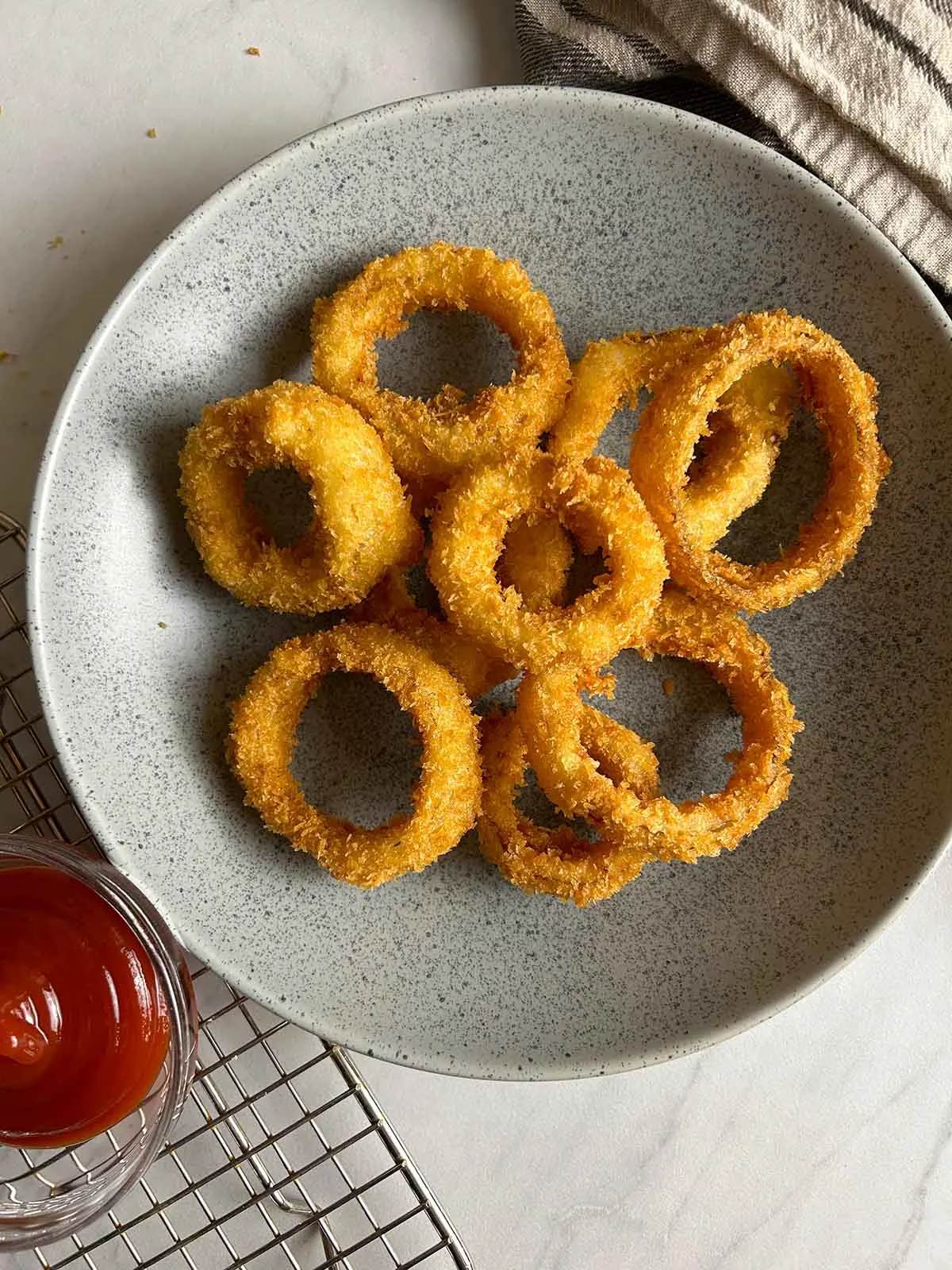 A plate of crispy onion rings with a small dish of ketchup on the side. 