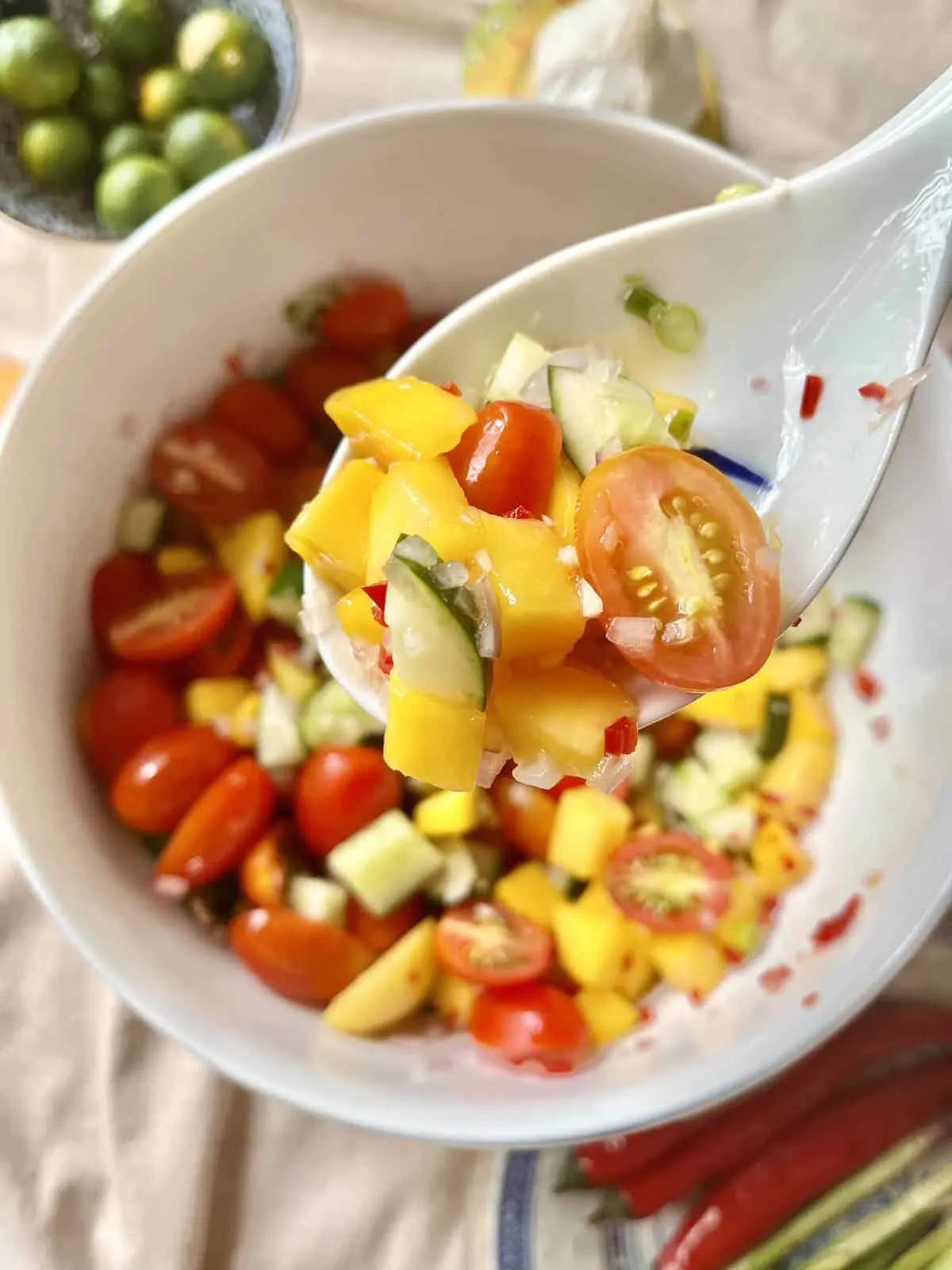 A spoon scooping some of the mango cucumber fruit salad out of a bowl. 