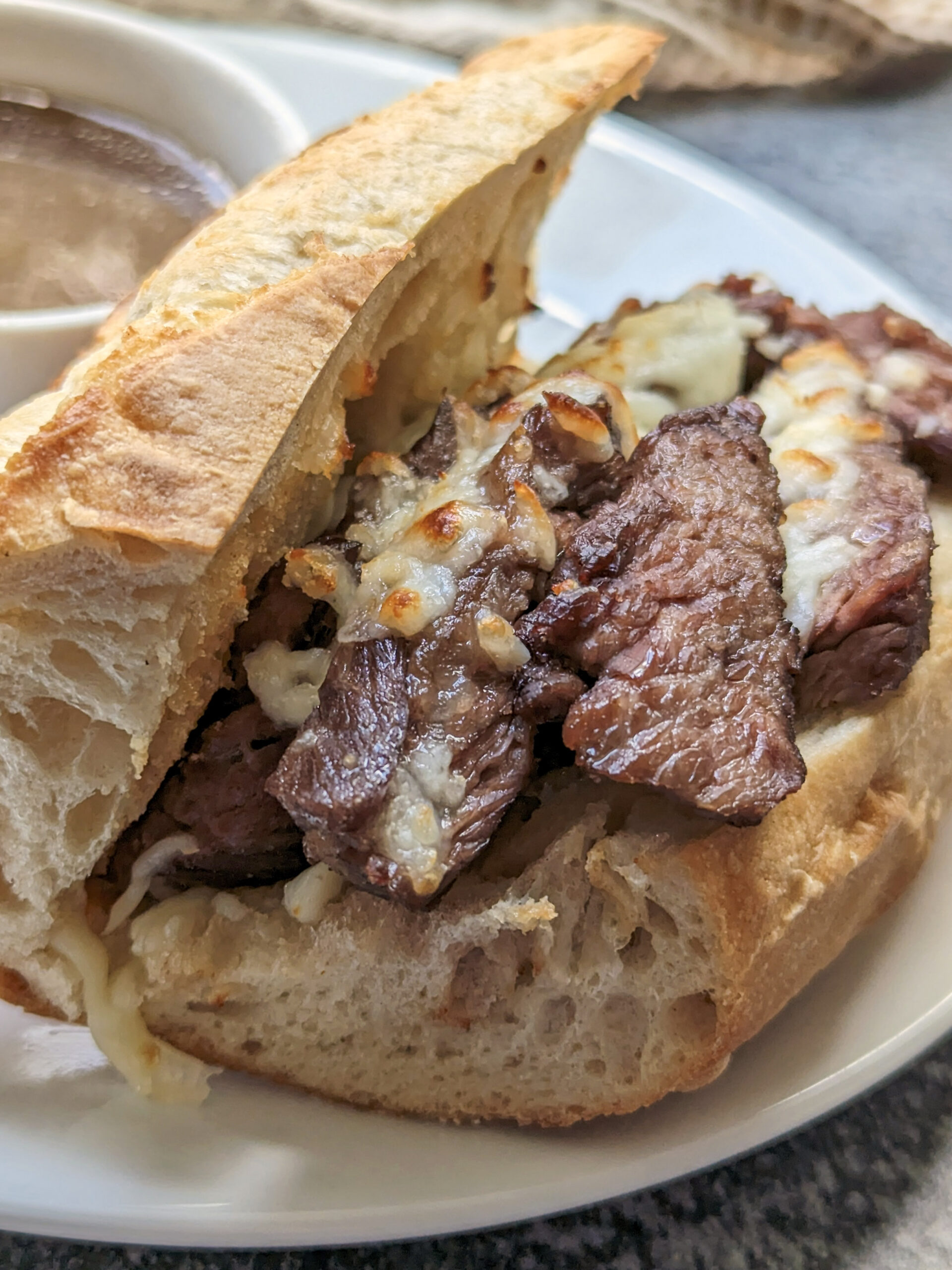 A french dip sandwich with au jus in the background. 
