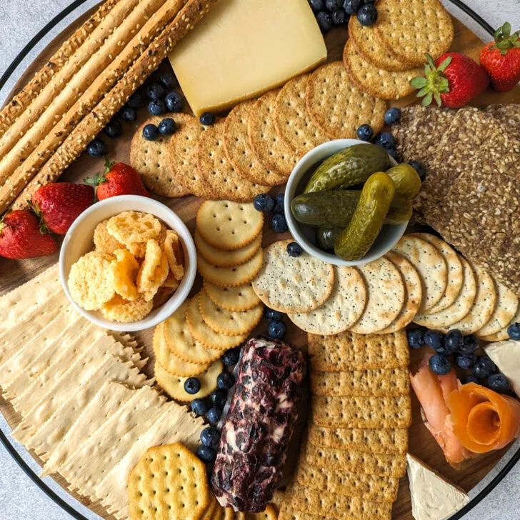 Best crackers for a charcuterie board on a board with fruit, pickles, and cheese.