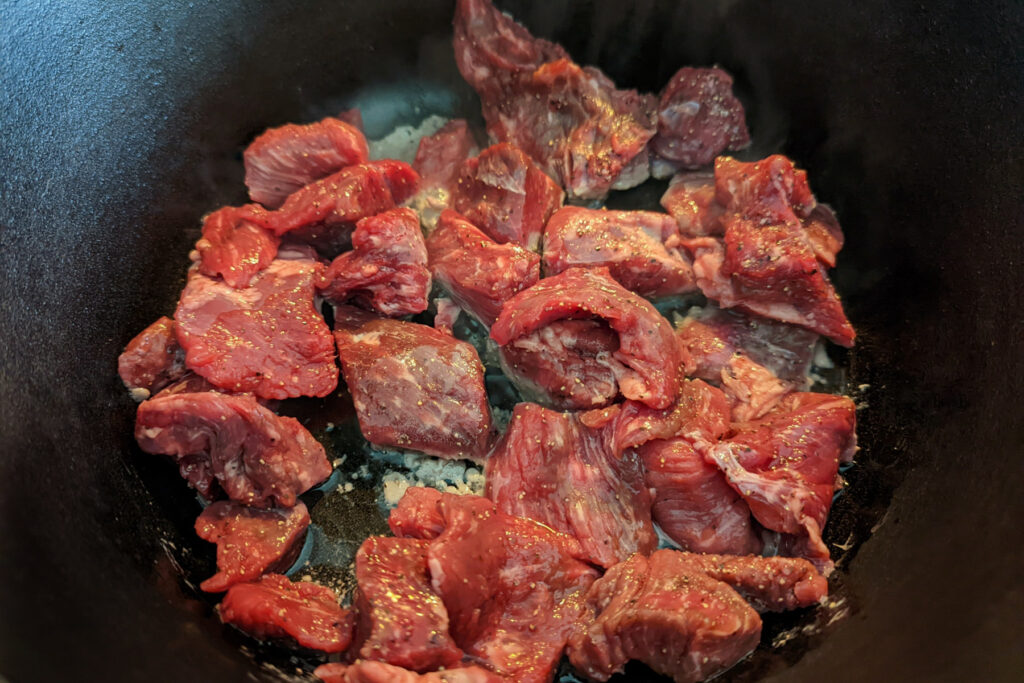 Pieces of beef chuck searing in hot oil in a pan.