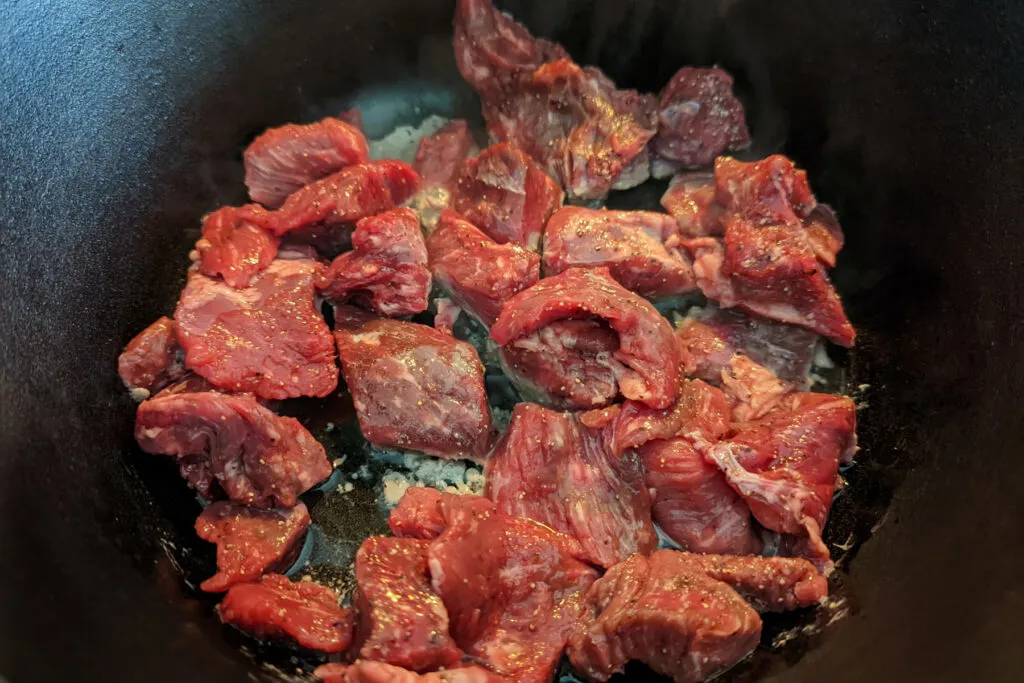 Pieces of beef chuck searing in hot oil in a pan.