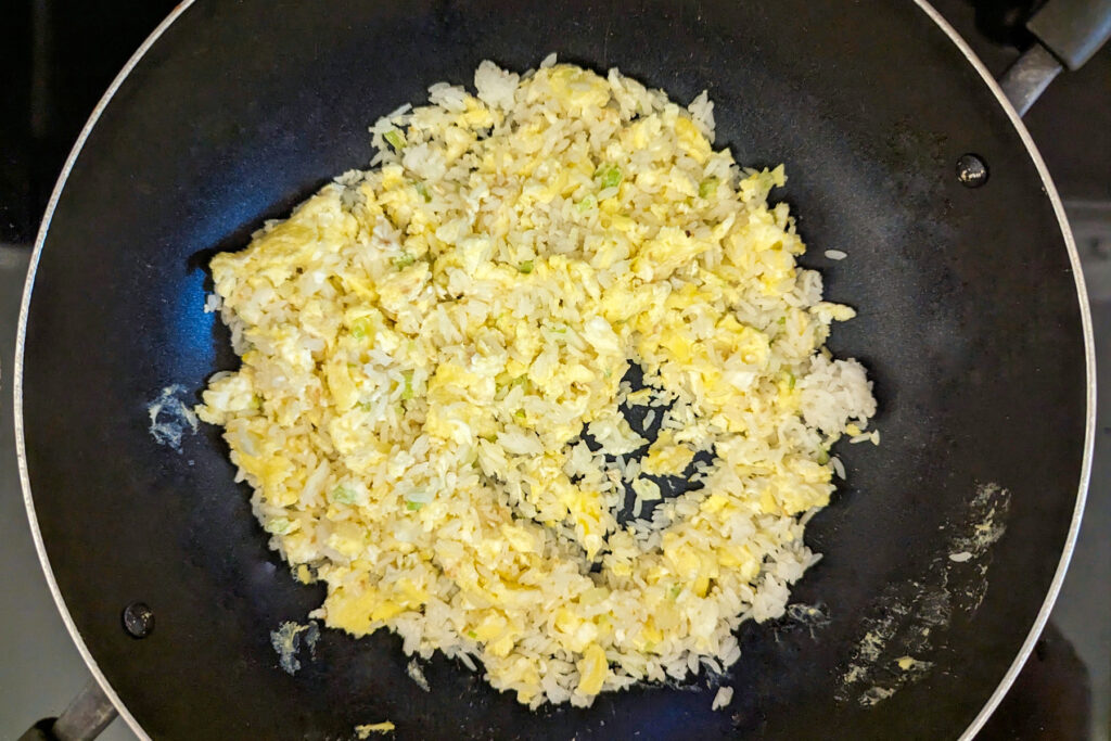 Leftover rice added to the eggs in a wok.