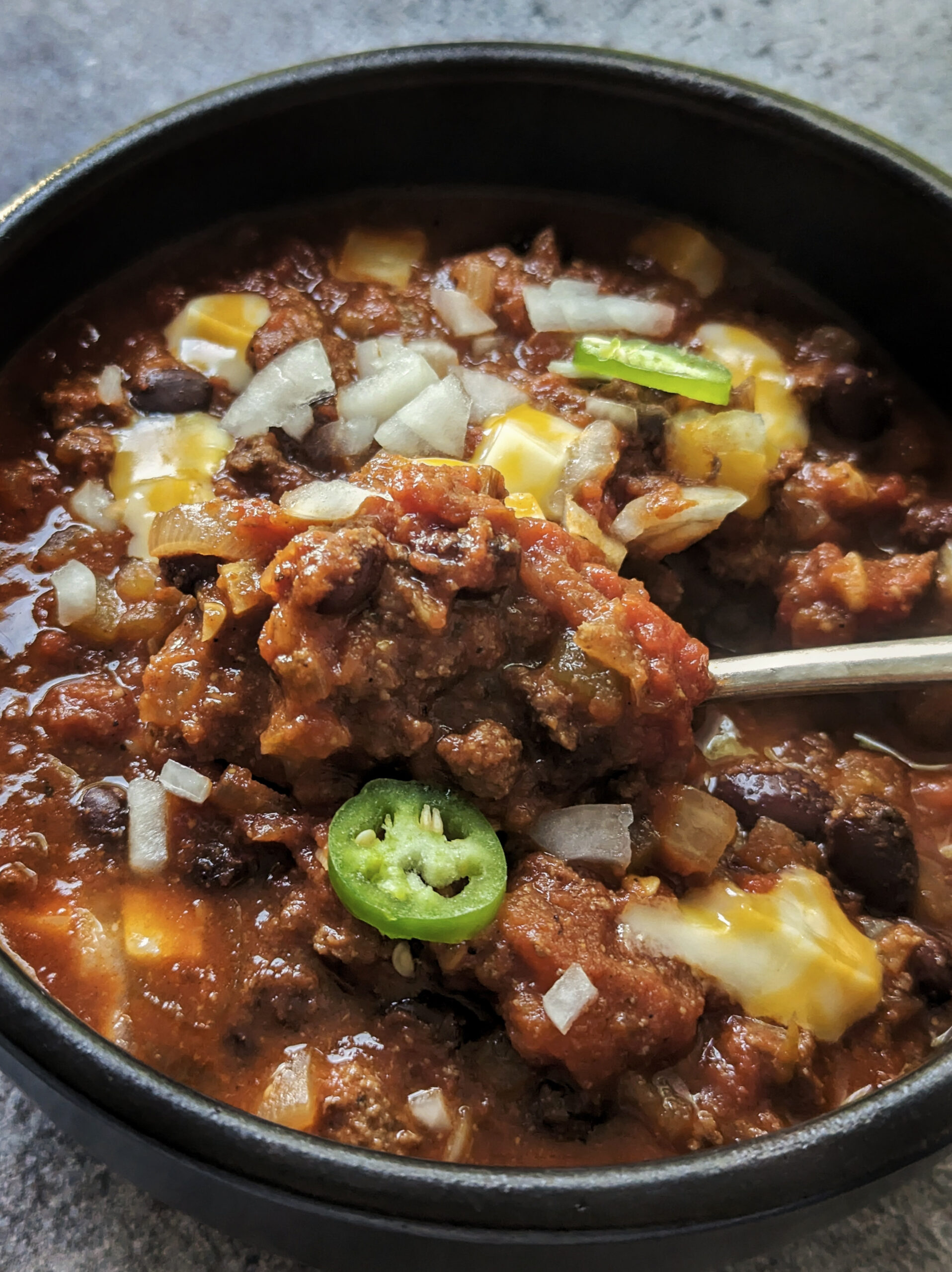A bowl of elk chili topped with onions, chilies, and cubed cheese.