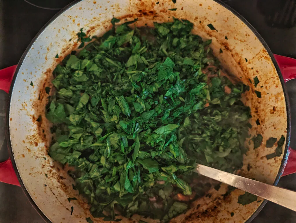 Spinach stirred into the cooking goat.