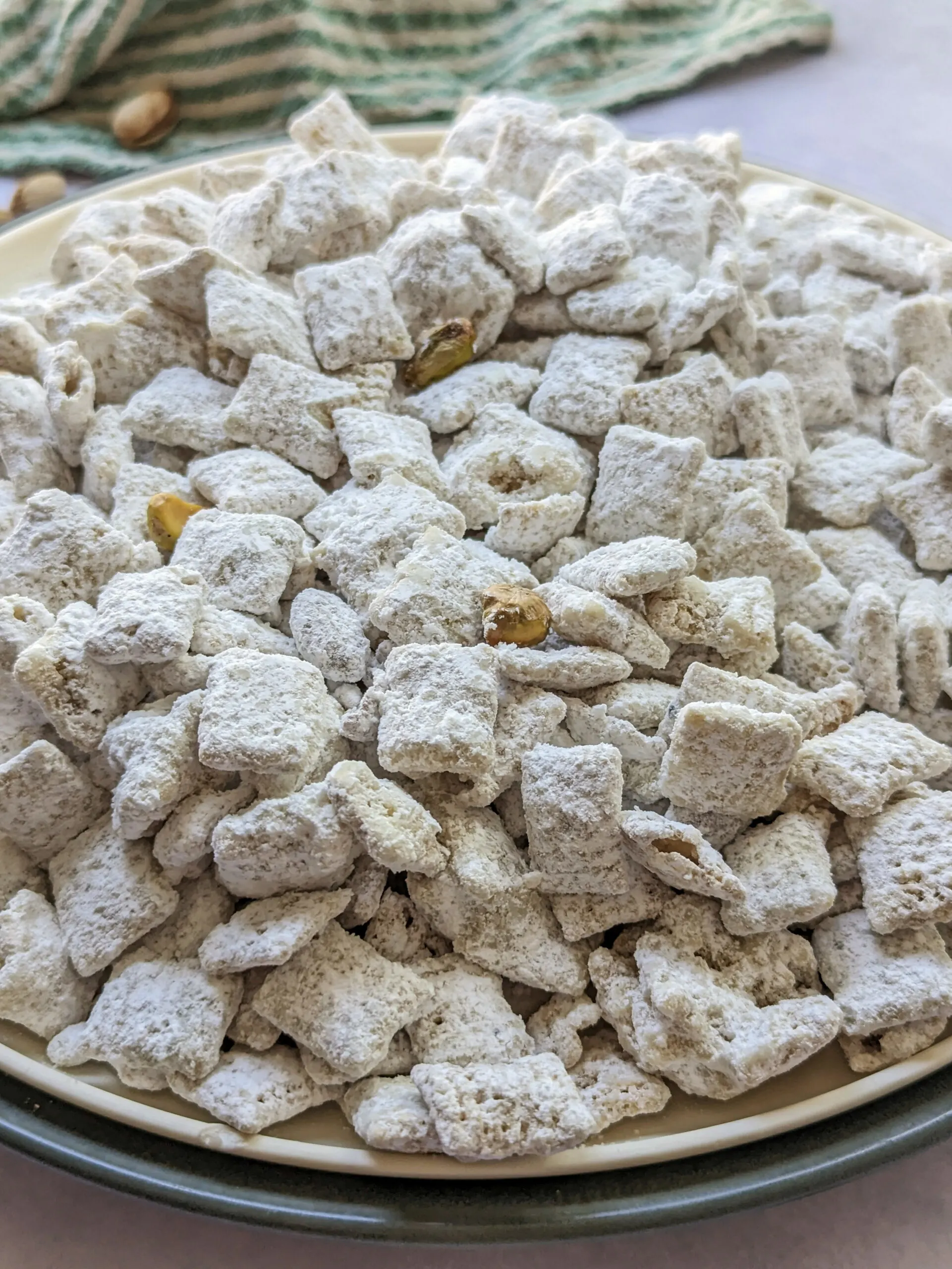 Pistachio puppy chow on a plate with pistachios in the background.