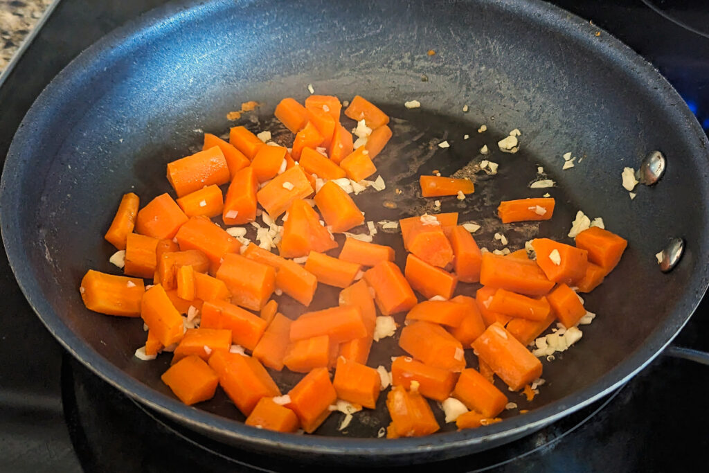 Carrots and garlic searing in a pan.