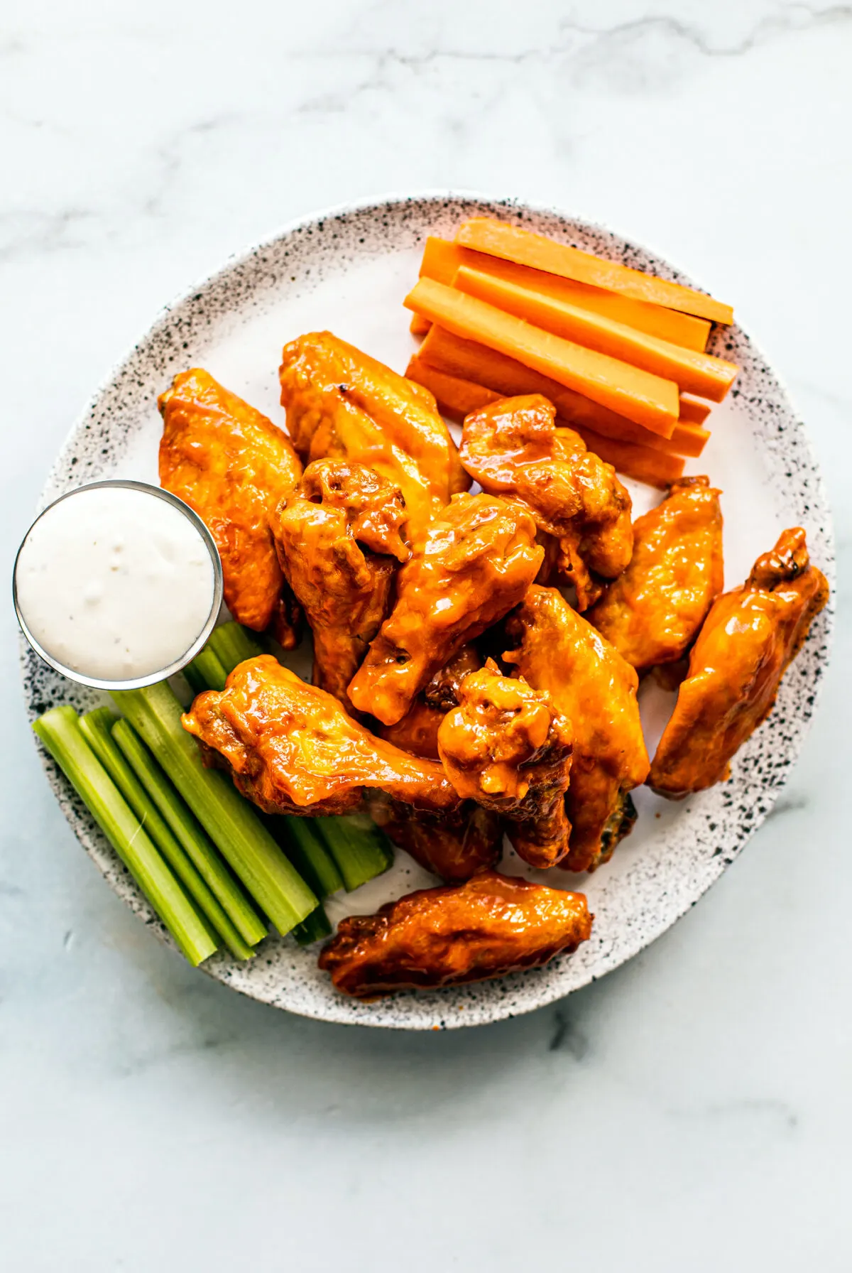 A plate of buffalo wings with vegetables.