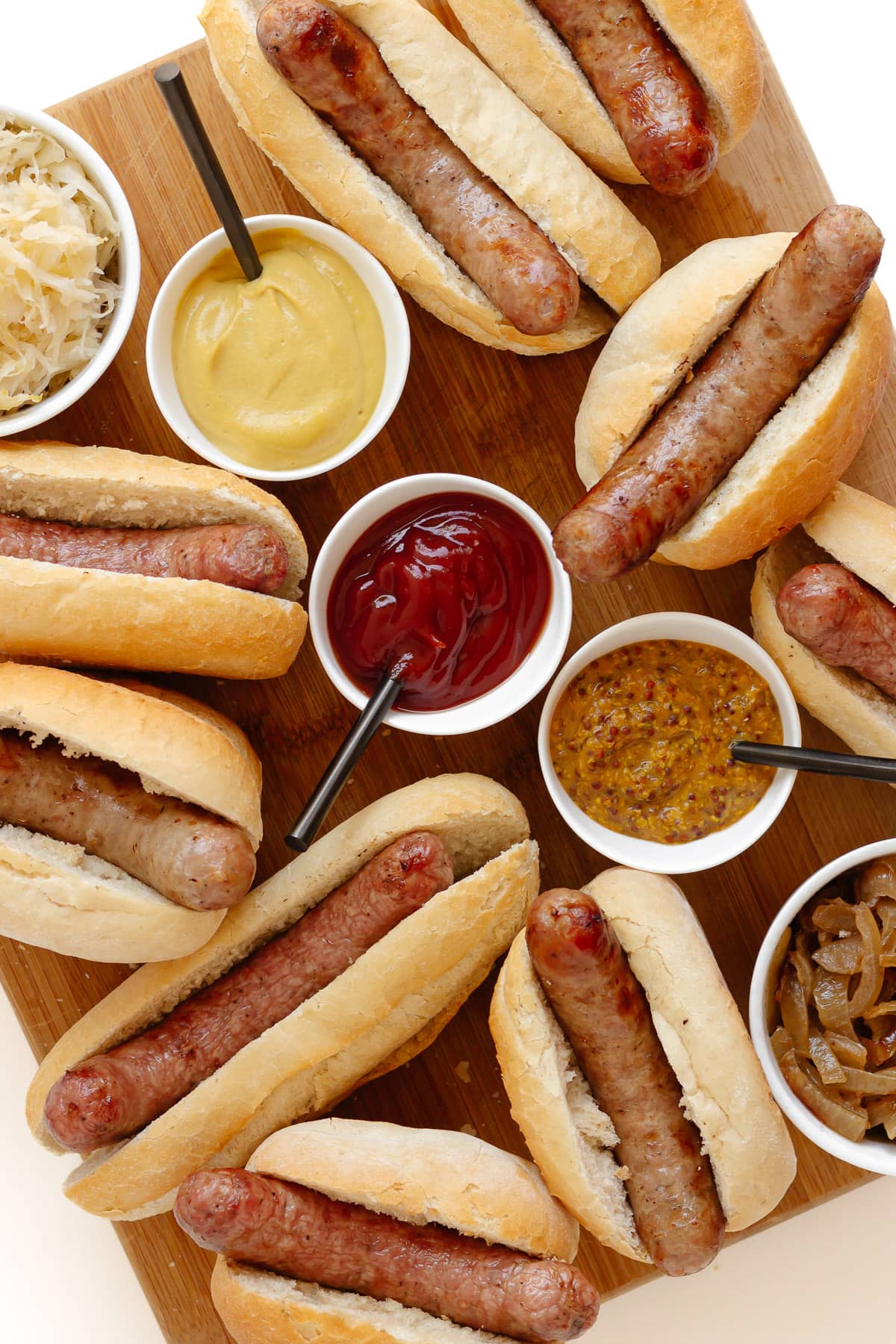 A tray of grilled bratwurst in buns with all the toppings. 