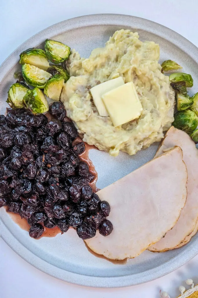 Mashed potatoes, turkey, cranberry sauce and brussel sprouts on a plate.