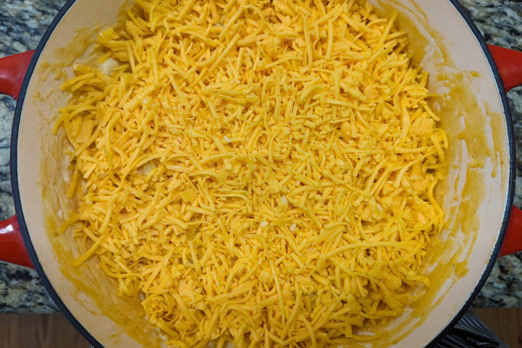 Dutch oven mac and cheese topped with shredded cheese.