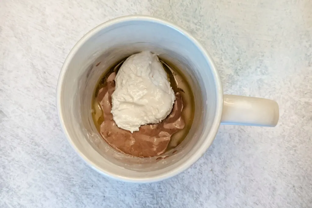 Some of the batter in a mug topped with marshmallow creme.