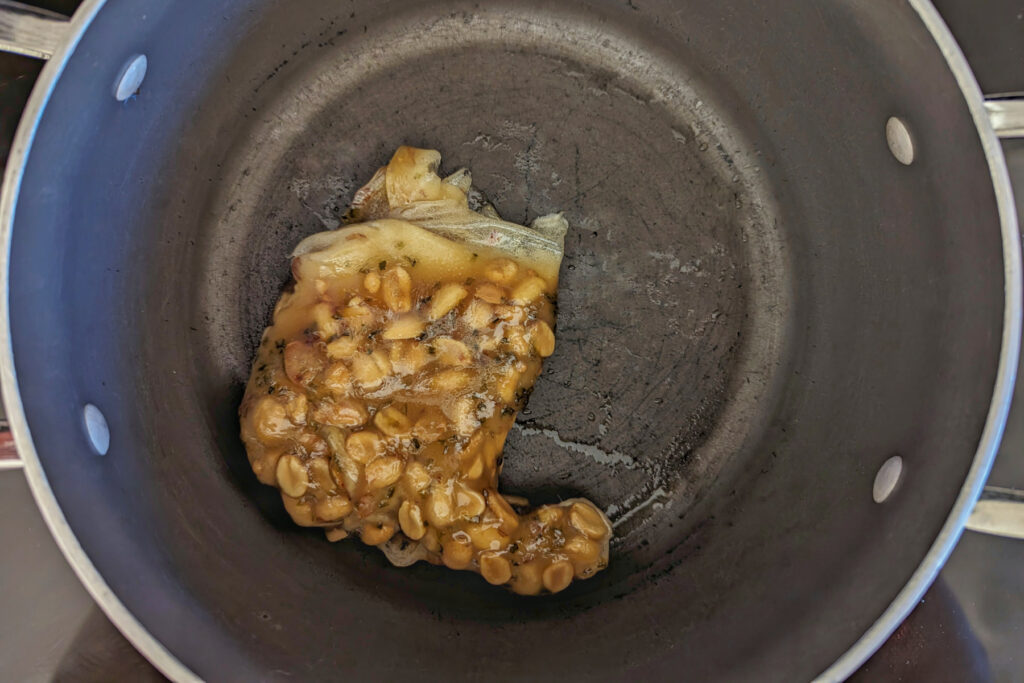 One section of peanut brittle added to a saucepan. 