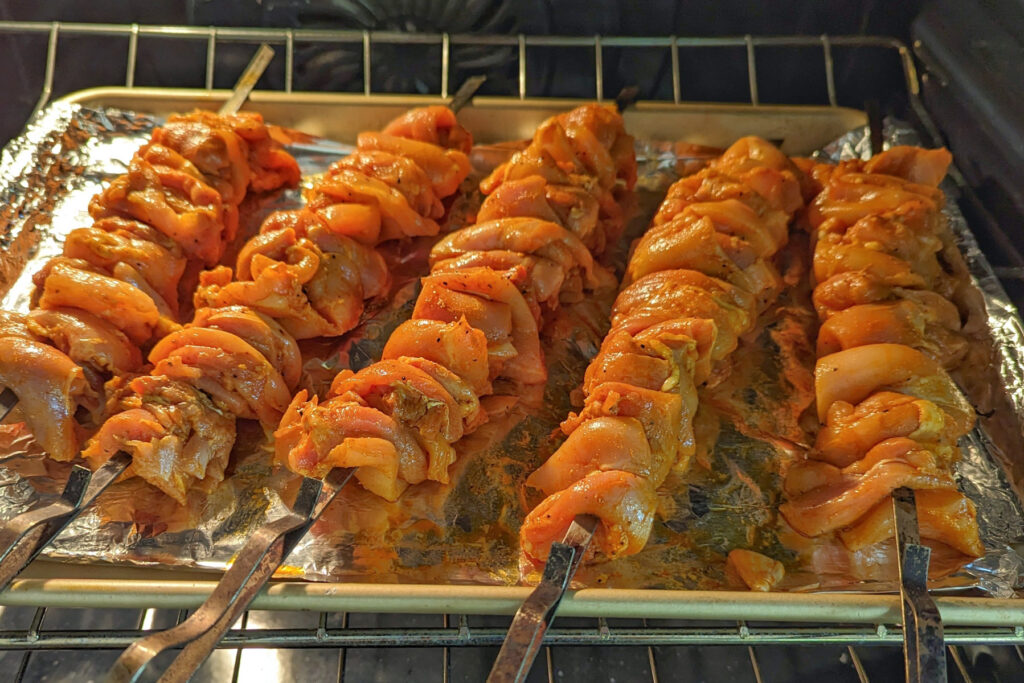 Chicken baking on skewers in the oven.