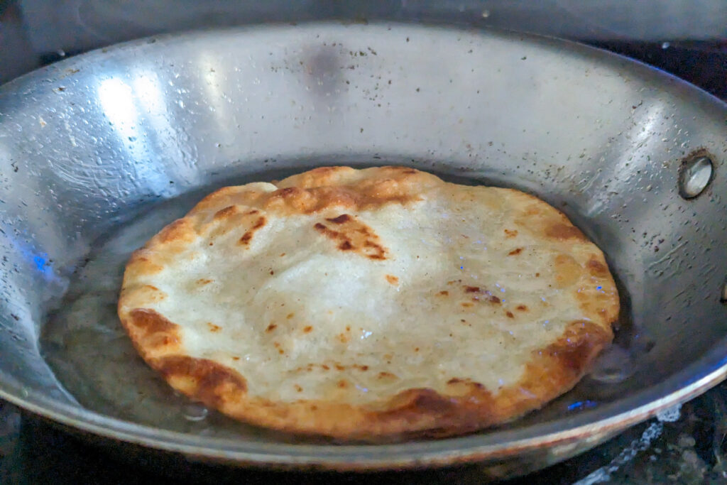 Corn tortillas frying in a pan.