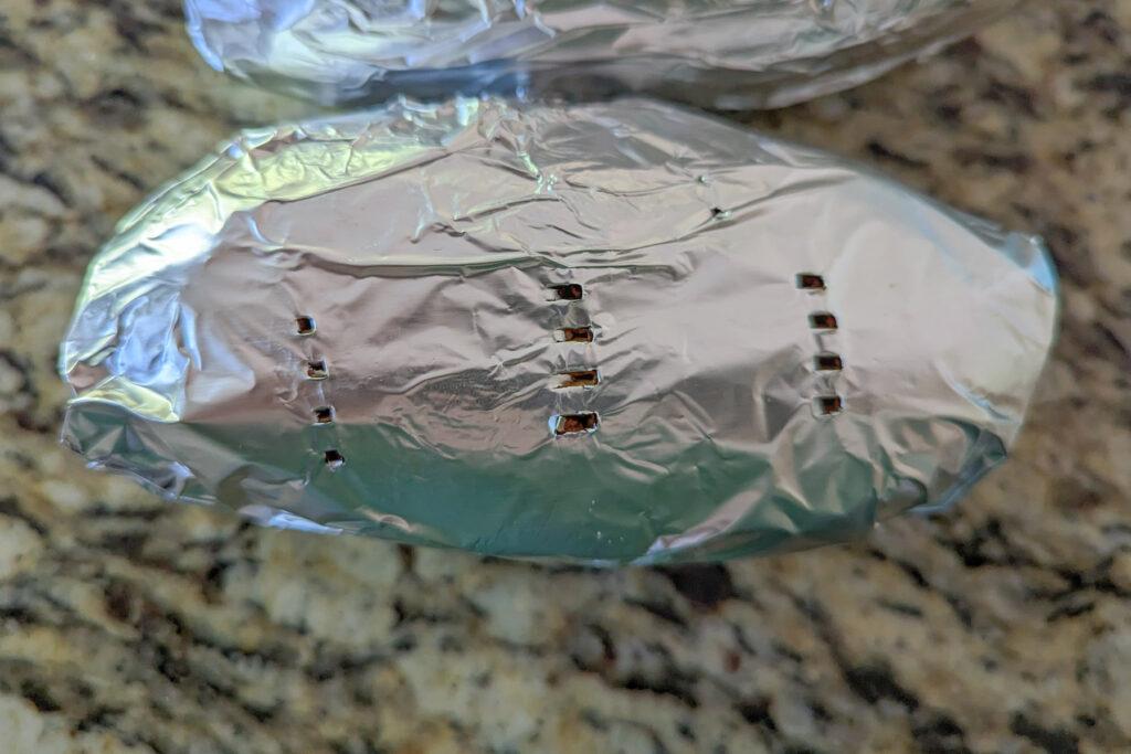 Sweet potato wrapped in foil with holes poked into it.