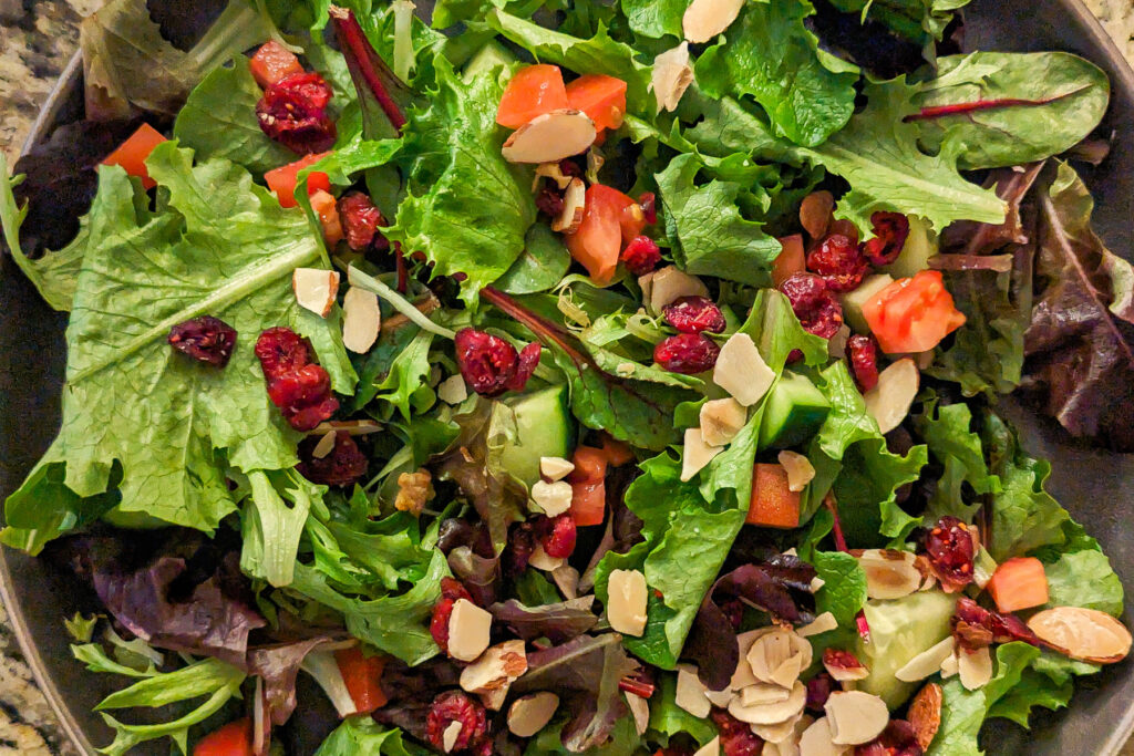 Mixed greens, tomatoes, cucumbers, nuts, and cranberries on a plate.