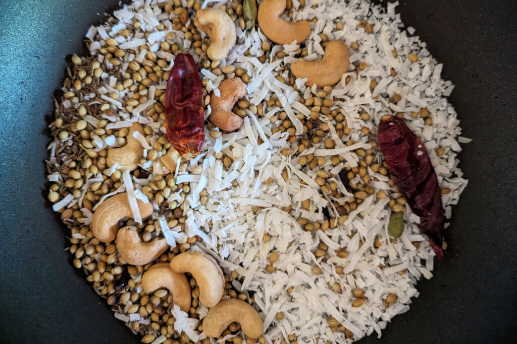 Whole spices, cashews, and coconut toasting in a pan.
