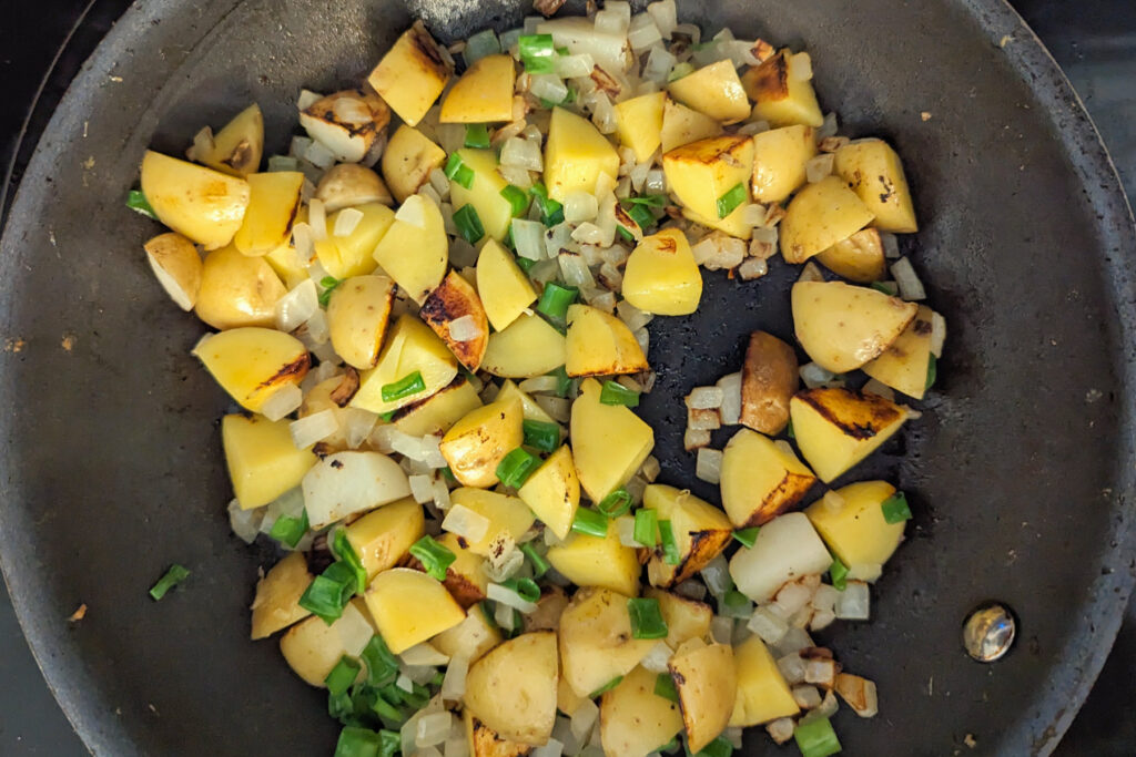 Potatoes cooking in a pan with vegetables.